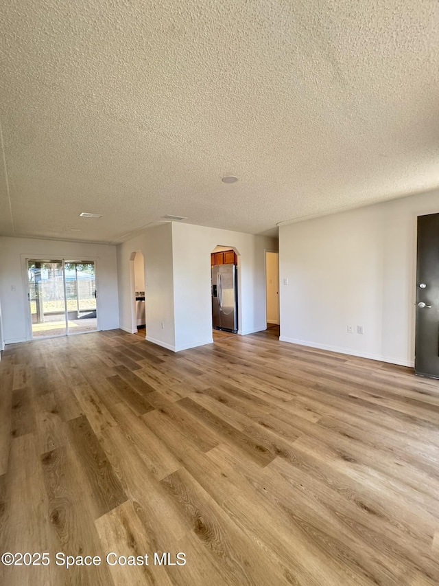 unfurnished living room with arched walkways, baseboards, a textured ceiling, and wood finished floors