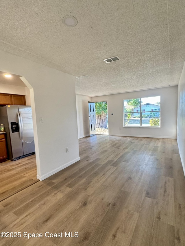 unfurnished living room with light wood-type flooring, arched walkways, a textured ceiling, and baseboards