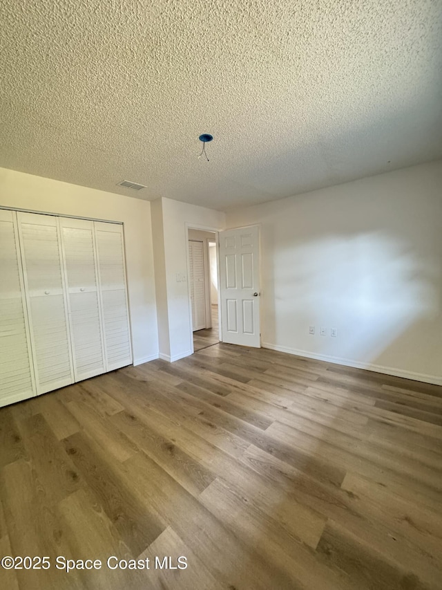 unfurnished bedroom with baseboards, a closet, a textured ceiling, and wood finished floors