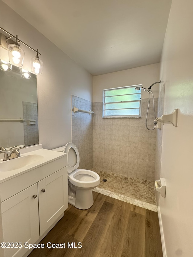 bathroom featuring toilet, a tile shower, wood finished floors, and vanity