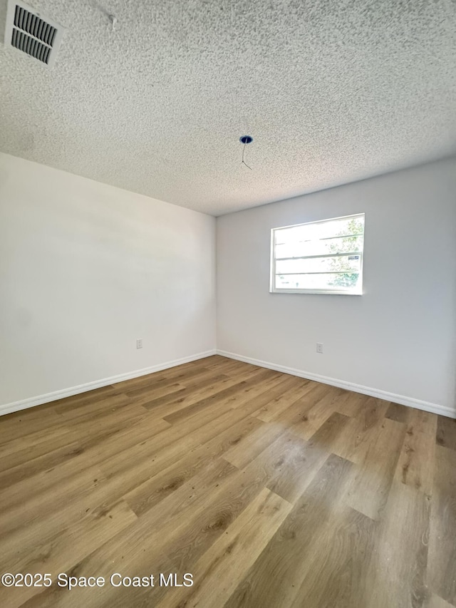 spare room featuring wood finished floors, baseboards, a textured ceiling, and visible vents