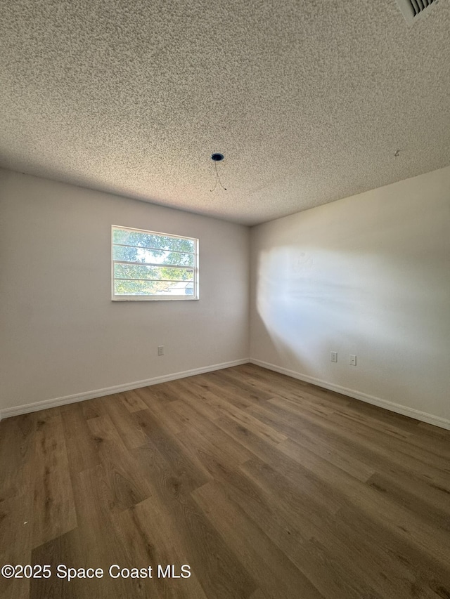 unfurnished room featuring a textured ceiling, baseboards, and wood finished floors