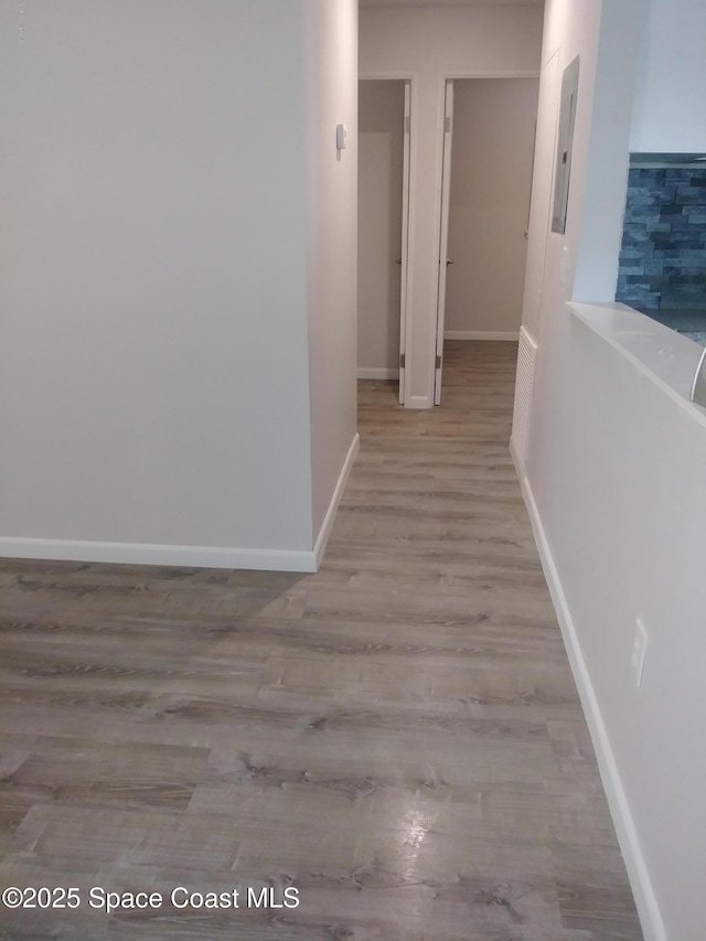 hallway featuring baseboards, electric panel, and wood finished floors