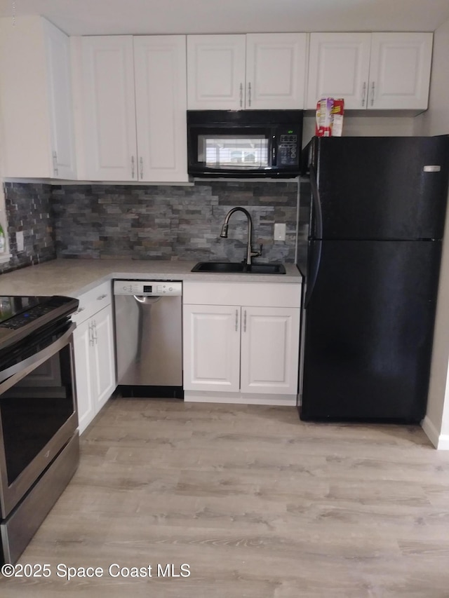 kitchen featuring white cabinets, a sink, light wood-type flooring, tasteful backsplash, and black appliances