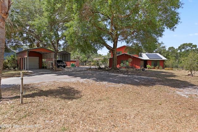 view of front of property with a detached carport, solar panels, an outbuilding, and driveway