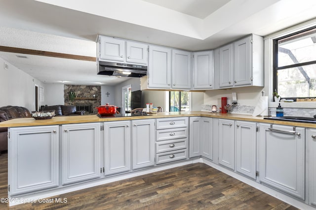 kitchen with a healthy amount of sunlight, black electric stovetop, butcher block counters, under cabinet range hood, and open floor plan