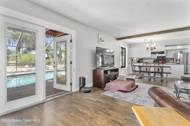 living area featuring a healthy amount of sunlight, wood finished floors, a textured ceiling, and a notable chandelier