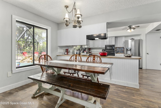 dining space featuring a textured ceiling, baseboards, ceiling fan with notable chandelier, and wood finished floors