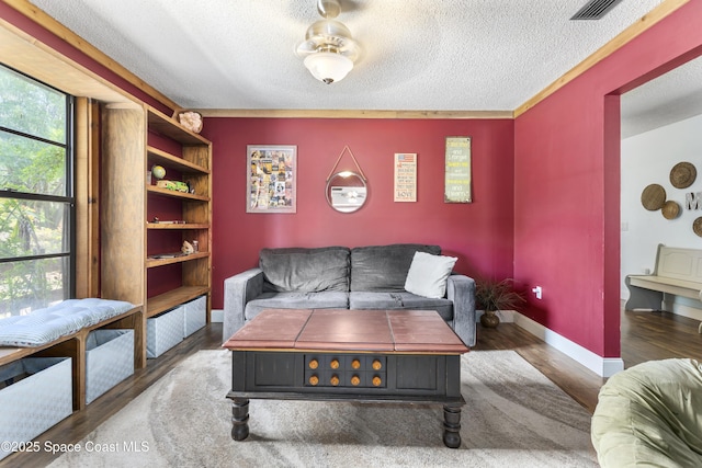 living room with baseboards, visible vents, a textured ceiling, and wood finished floors
