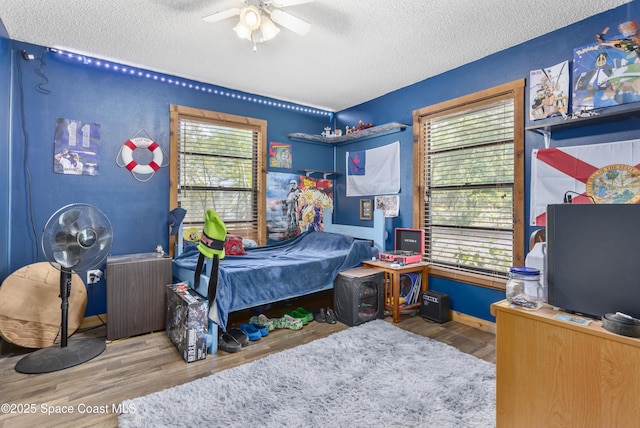 bedroom featuring baseboards, a textured ceiling, ceiling fan, and wood finished floors