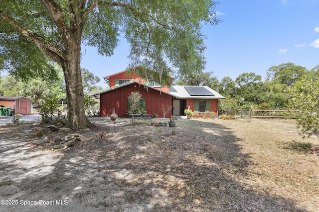view of front of home with fence, an outdoor structure, solar panels, and a storage shed
