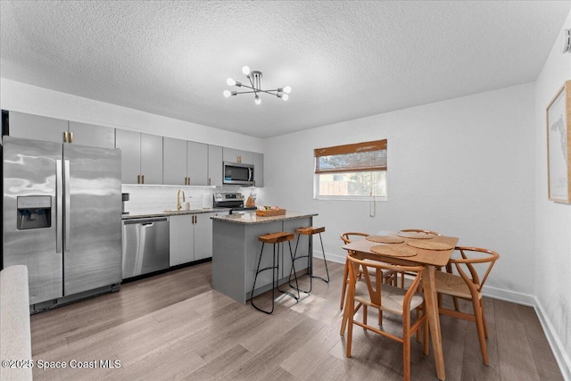 299 E Central Blvd Unit 6, Cape Canaveral, FL 32920 - kitchen with gray cabinets, a kitchen island, appliances with stainless steel finishes, a chandelier, and light wood-style flooring