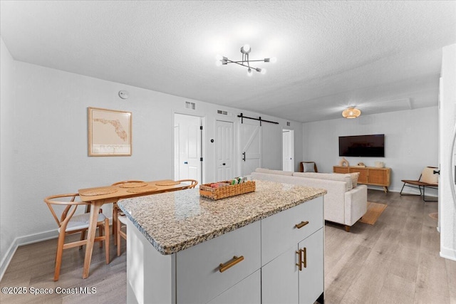299 E Central Blvd Unit 6, Cape Canaveral, FL 32920 - kitchen with a textured ceiling, a center island, a barn door, baseboards, and light wood finished floors