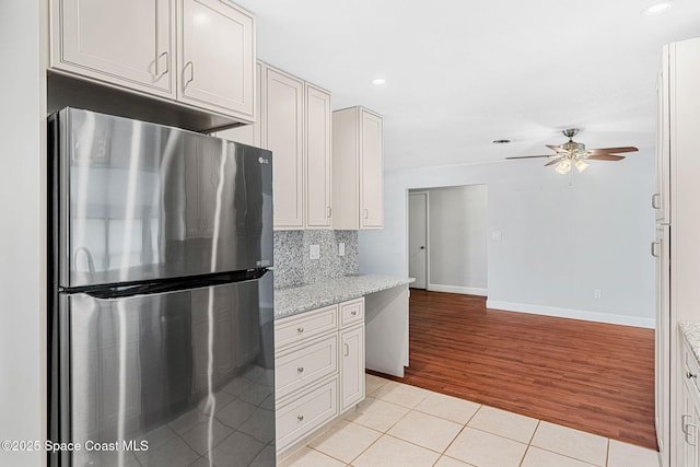 kitchen featuring freestanding refrigerator, a ceiling fan, baseboards, decorative backsplash, and light tile patterned floors