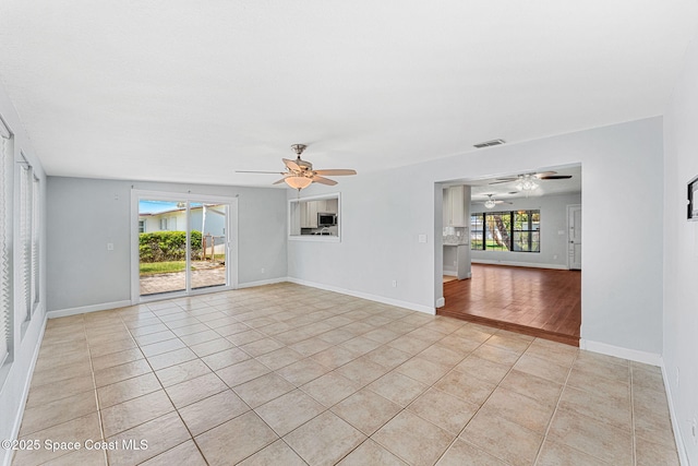 empty room with baseboards, ceiling fan, visible vents, and light tile patterned floors