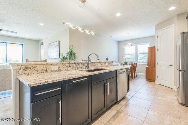 7447 Bluemink Ln, Melbourne, FL 32940 - kitchen featuring a sink, appliances with stainless steel finishes, a textured ceiling, light stone counters, and an island with sink