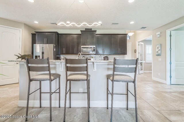 7447 Bluemink Ln, Melbourne, FL 32940 - kitchen with appliances with stainless steel finishes, a center island with sink, a breakfast bar, tasteful backsplash, and a textured ceiling