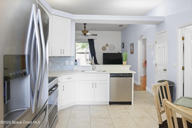 kitchen featuring ceiling fan, arched walkways, a sink, appliances with stainless steel finishes, and backsplash