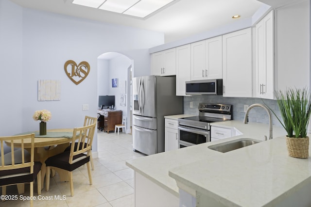kitchen featuring appliances with stainless steel finishes, tasteful backsplash, arched walkways, a sink, and light tile patterned floors