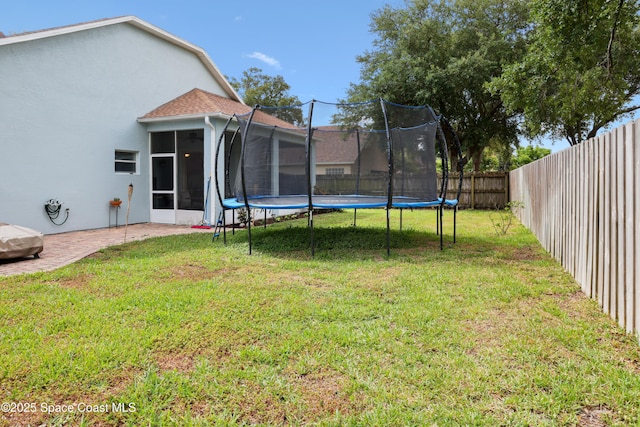view of yard featuring a sunroom, a patio, a fenced backyard, and a trampoline