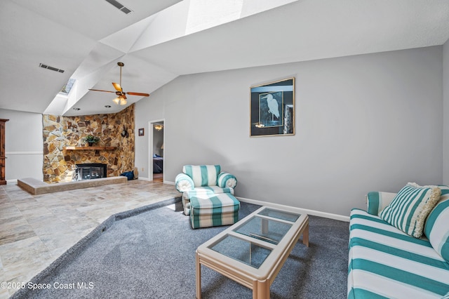 living area featuring ceiling fan, vaulted ceiling, a skylight, a stone fireplace, and baseboards