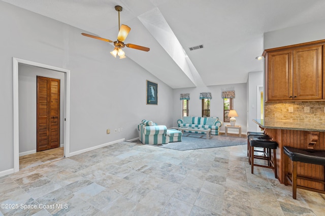 living room with ceiling fan, stone finish floors, baseboards, and high vaulted ceiling