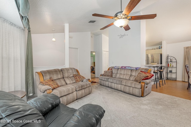 carpeted living area with a ceiling fan, vaulted ceiling, wood finished floors, and visible vents