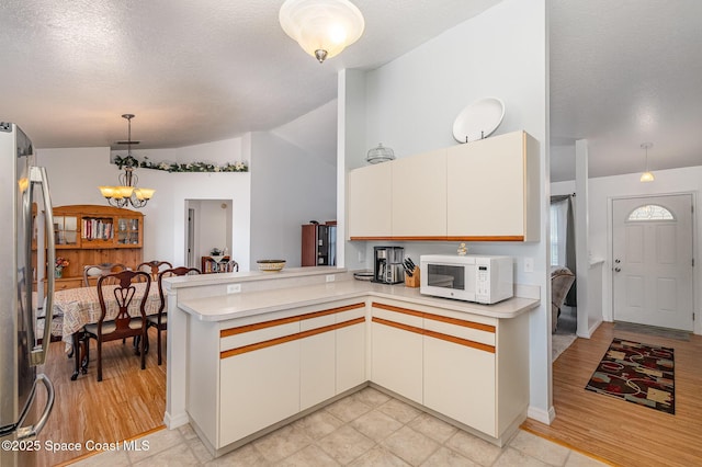 kitchen featuring vaulted ceiling, light countertops, white microwave, freestanding refrigerator, and a peninsula