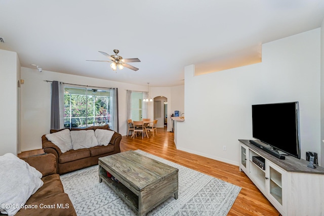 living area with arched walkways, baseboards, light wood-style flooring, and ceiling fan with notable chandelier