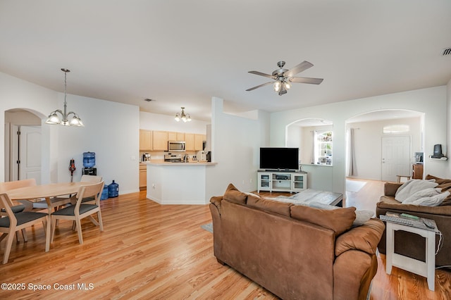 living room with light wood-style floors, arched walkways, ceiling fan with notable chandelier, and visible vents