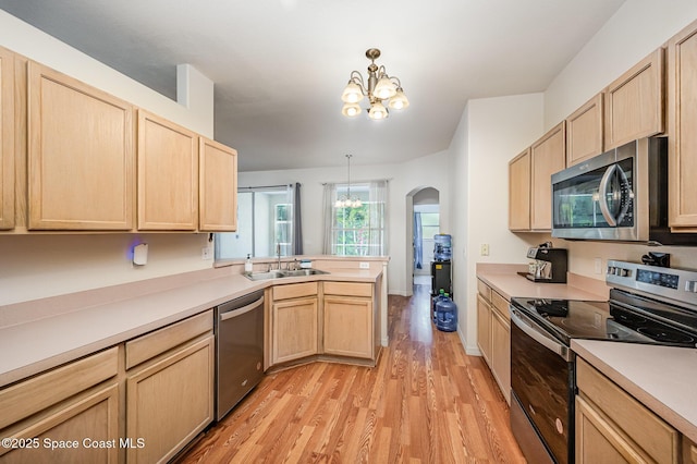 kitchen with appliances with stainless steel finishes, a sink, light brown cabinets, arched walkways, and a chandelier