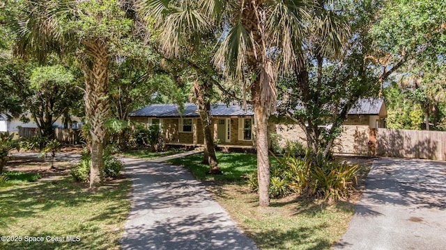 obstructed view of property with fence, metal roof, and driveway