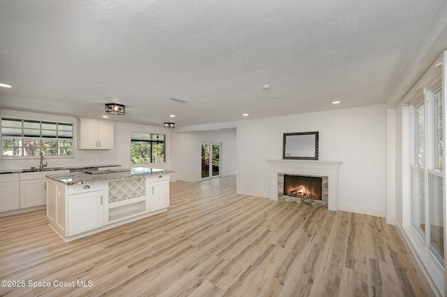 kitchen with a kitchen island, white cabinetry, a sink, open floor plan, and light wood-style flooring