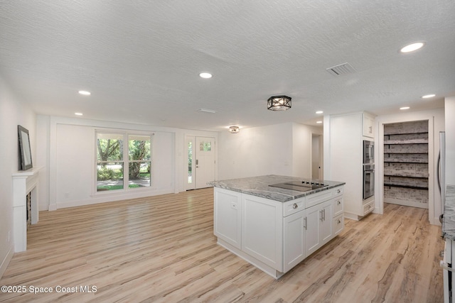 kitchen with a textured ceiling, visible vents, appliances with stainless steel finishes, light wood-style flooring, and white cabinetry