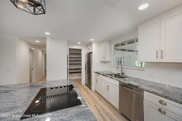 kitchen with light wood-type flooring, a sink, stone countertops, white cabinets, and stainless steel appliances