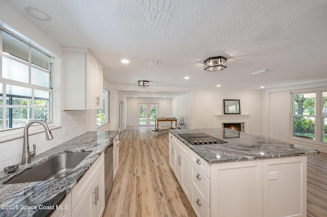 kitchen with a textured ceiling, black electric cooktop, a sink, white cabinets, and light wood finished floors