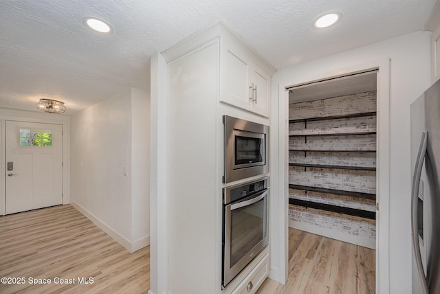 kitchen featuring baseboards, light wood-type flooring, a textured ceiling, white cabinets, and stainless steel appliances