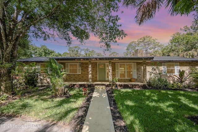 single story home featuring covered porch, brick siding, a chimney, and a lawn
