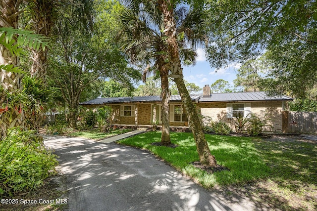 ranch-style house with fence, a front lawn, brick siding, a chimney, and metal roof