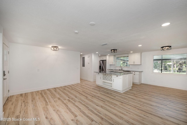 kitchen featuring open floor plan, stainless steel refrigerator with ice dispenser, light wood-type flooring, white cabinets, and a sink