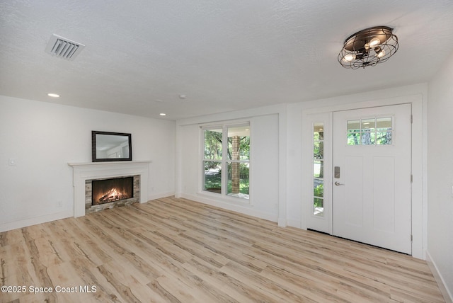 foyer entrance with a warm lit fireplace, visible vents, baseboards, and light wood finished floors