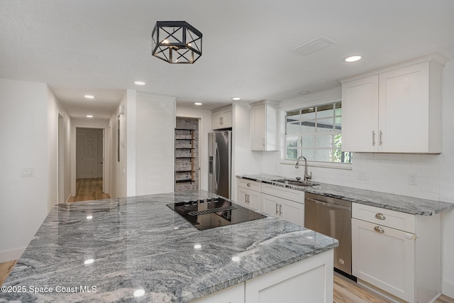 kitchen with a sink, light wood-style flooring, stainless steel appliances, tasteful backsplash, and visible vents