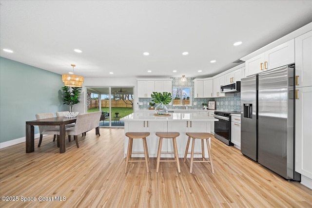 2059 Barracuda Ave, Melbourne Beach, FL 32951 - kitchen featuring decorative backsplash, a center island, white cabinetry, light wood finished floors, and appliances with stainless steel finishes