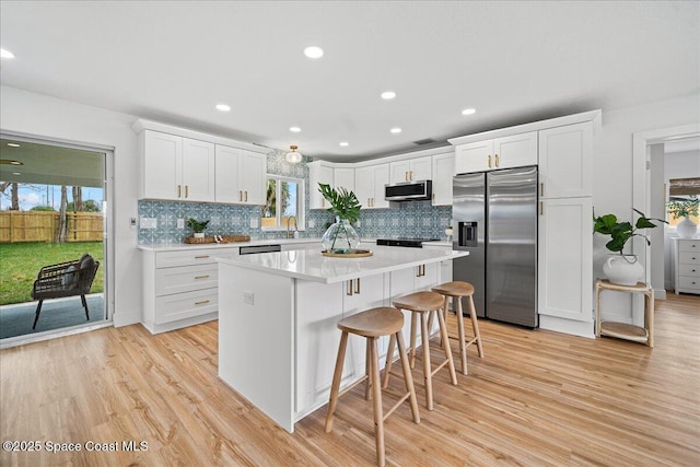 2059 Barracuda Ave, Melbourne Beach, FL 32951 - kitchen featuring stainless steel appliances, decorative backsplash, light wood-style flooring, and white cabinetry