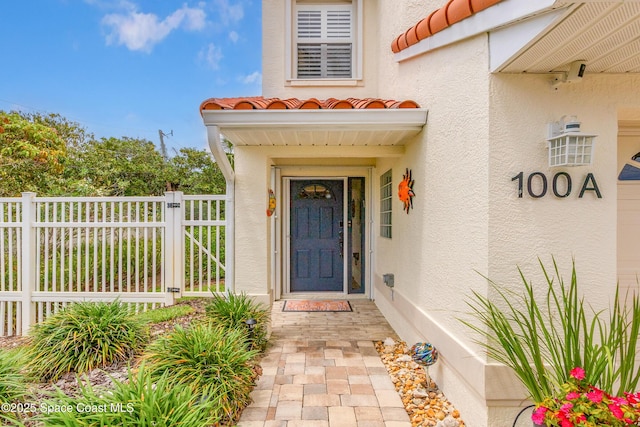 doorway to property featuring stucco siding, a tiled roof, and fence