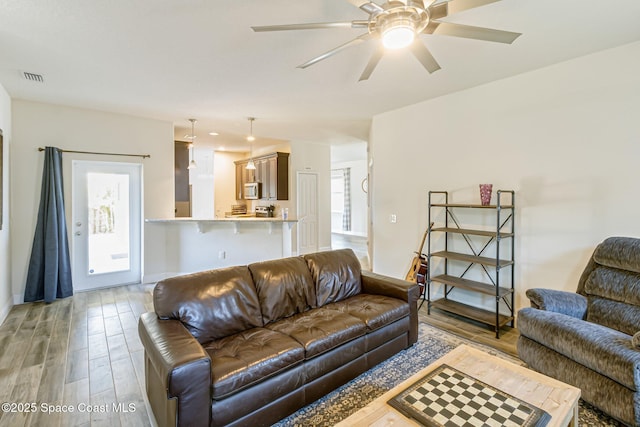 living room with visible vents, light wood finished floors, ceiling fan, and baseboards