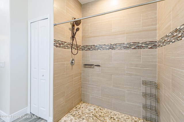 full bathroom featuring baseboards, a tile shower, and a closet