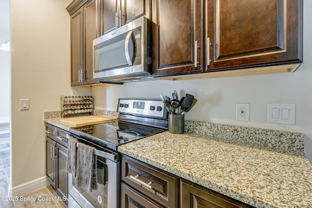 kitchen with stainless steel appliances, dark brown cabinetry, light stone countertops, and baseboards