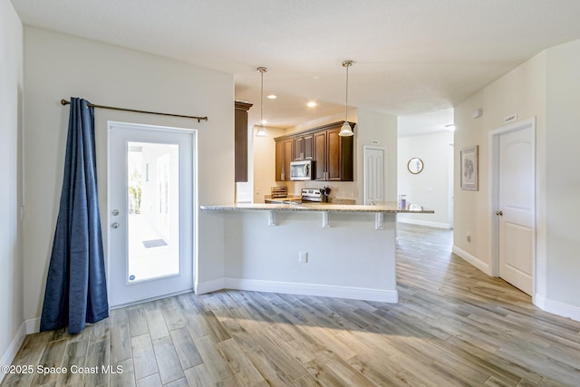 kitchen with appliances with stainless steel finishes, light wood-type flooring, baseboards, light stone counters, and a breakfast bar
