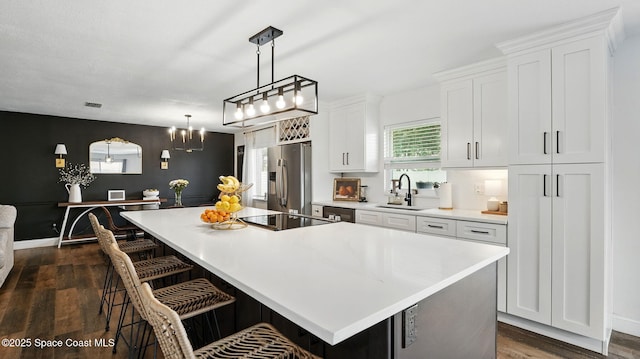 kitchen with a kitchen island, black electric cooktop, a sink, stainless steel fridge, and white cabinetry
